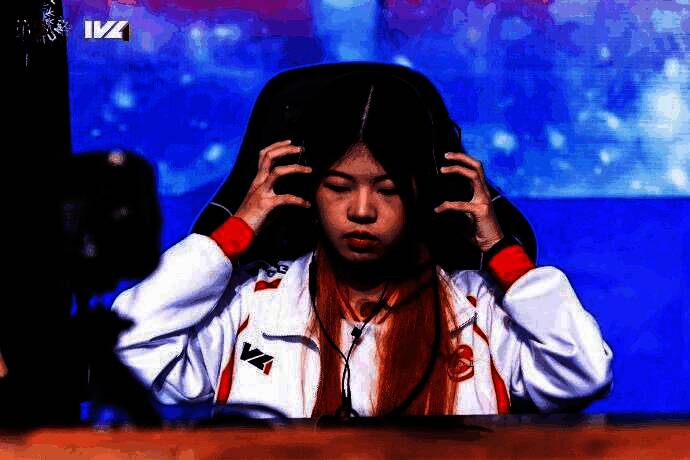 GG_violet选手专注比赛中的特写镜头,眼神坚定,耳机微斜,背景为赛事现场灯光与屏幕画面