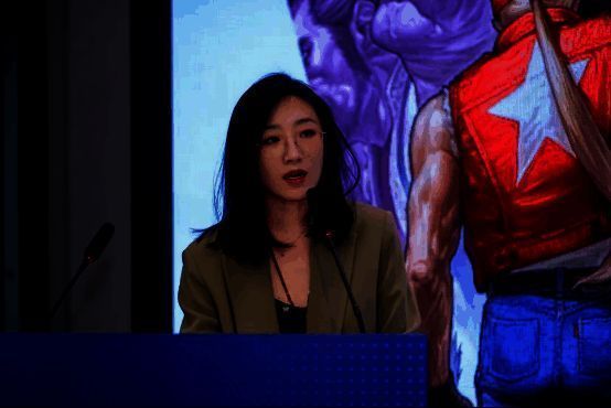 张旭在台上介绍石景山区产业布局,背景为区域发展规划图与游戏产业园区实景