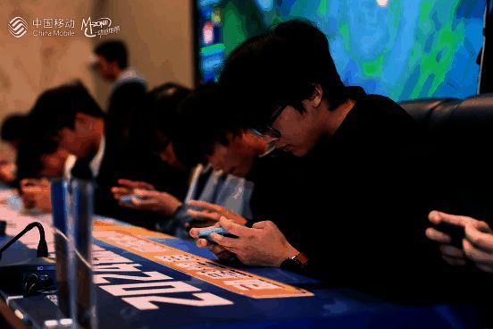 选手在比赛区专注操作手机,周围环绕着裁判与工作人员,背景为大型赛事LOGO