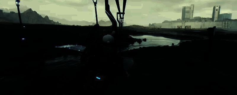 《死亡搁浅2》中主角手持消音狙击枪潜伏于山地环境,枪身细节清晰,背景为荒凉废土与远处敌人哨岗