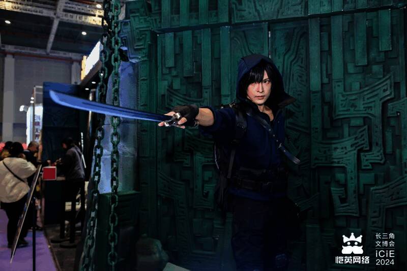 COSER扮演的张起灵与吴邪站立于展台中央,周围粉丝举手机拍摄,气氛热烈