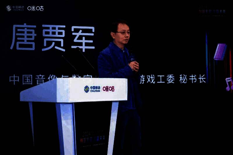 唐贾军在论坛上发表演讲,背景大屏展示2024年中国游戏市场数据图表,包括收入与用户增长趋势