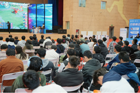 高校电竞公开课现场：PEL职业教练在兰州大学报告厅演示《和平精英》战术地图标记系统，台下百余名学生手持笔记本专注记录，投影幕布显示动态战术推演流程图